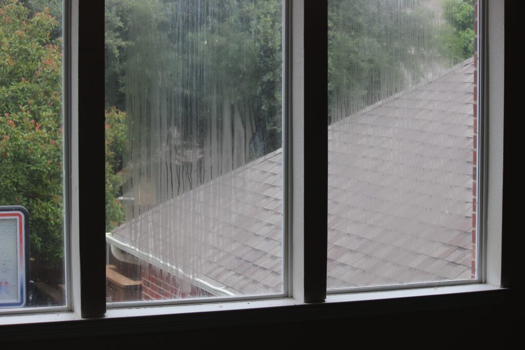 Rain-streaked window overlooking a shingled roof