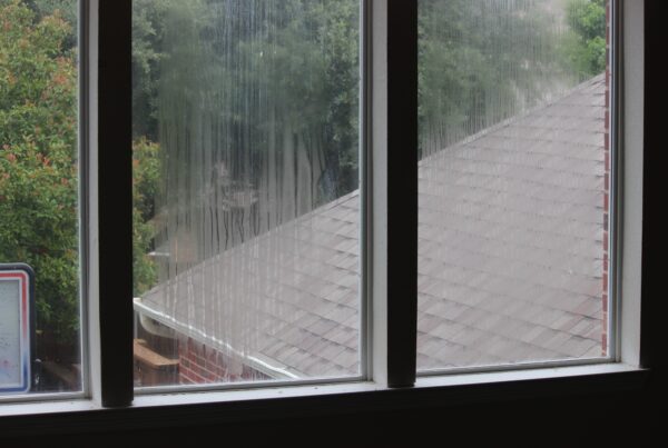 Rain-streaked window overlooking a shingled roof