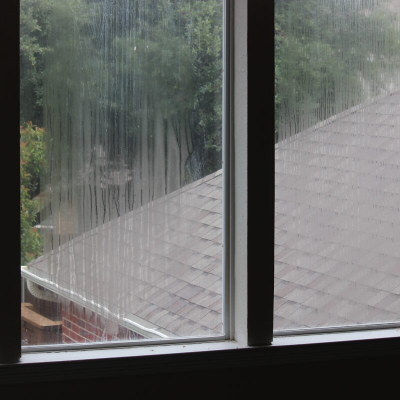 Rain-streaked window overlooking a shingled roof